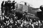 A gathering of men of No 467 Squadron, Royal Australian Air Force to celebrate the completion of 100 operations by the Avro Lancaster R5868/`PO-S' (S for Sugar) after its sortie on 11 - 12 May 1944 to a communications target in Belgium. Below the cockpit of the Lancaster are the emblems indicating the number of operational flights and the award of three DSOs and two DFCs to crew members