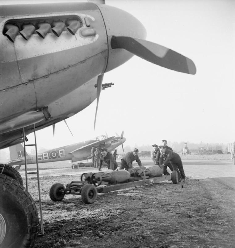 Armourers wheeling trolleys of 500-lb MC bombs to De Havilland Mosquito FB Mark VIs of No. 464 Squadron RAAF at Hunsdon, Hertfordshire. The further aircraft, MM412 'SB-F', survived the war to be sold to the Yugoslav Air Force in 1952.